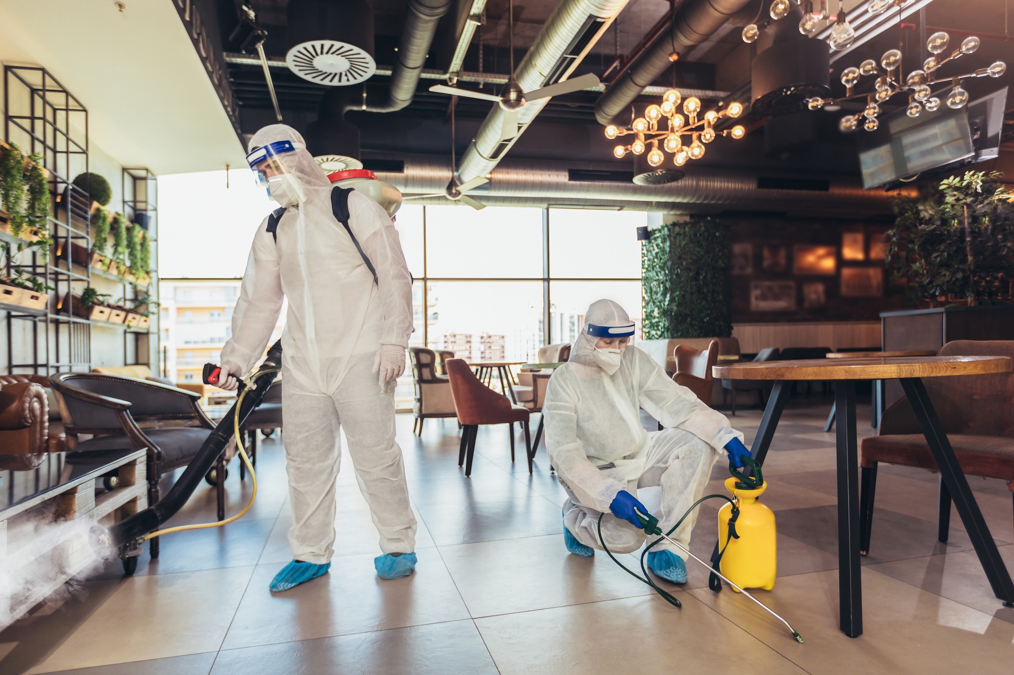 Professional workers in hazmat suits disinfecting indoor of cafe or restaurant, pandemic health risk, coronavirus